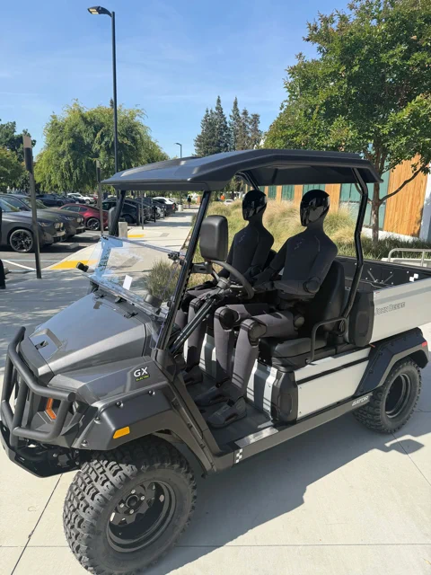Two Figure humanoid robots hitching a ride in a John Deere Gator utility vehicle